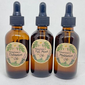 May include: Three amber glass bottles with dropper tops and labels. The labels are cream colored with a floral design and black text. The text on the labels reads "The Herbal Witch Co. Divination Oil", "The Herbal Witch Co. Full Moon Oil", and "The Herbal Witch Co. Meditation Oil".