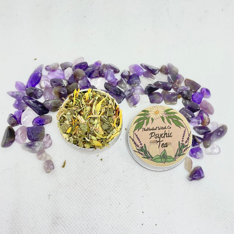 May include: A small tin of loose leaf tea with a label that reads "The Herbal Witch Co. Psychic Tea". The tin is surrounded by small purple amethyst stones.