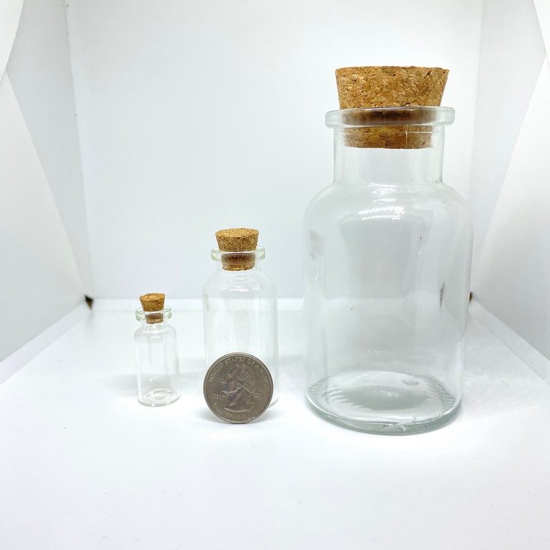 May include: Three glass bottles with cork stoppers. The bottles are clear and have a round shape. The bottles are of different sizes, with the largest bottle being about the size of a standard US quarter.