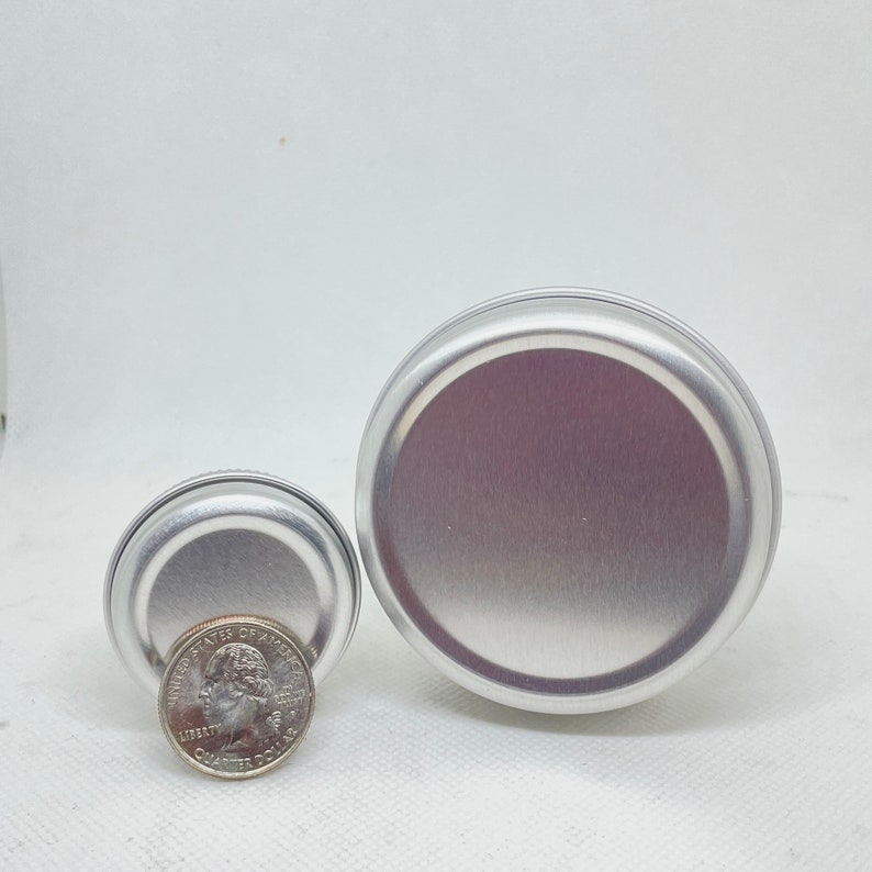 May include: Two silver metal tins with lids. The smaller tin is about the size of a US quarter.