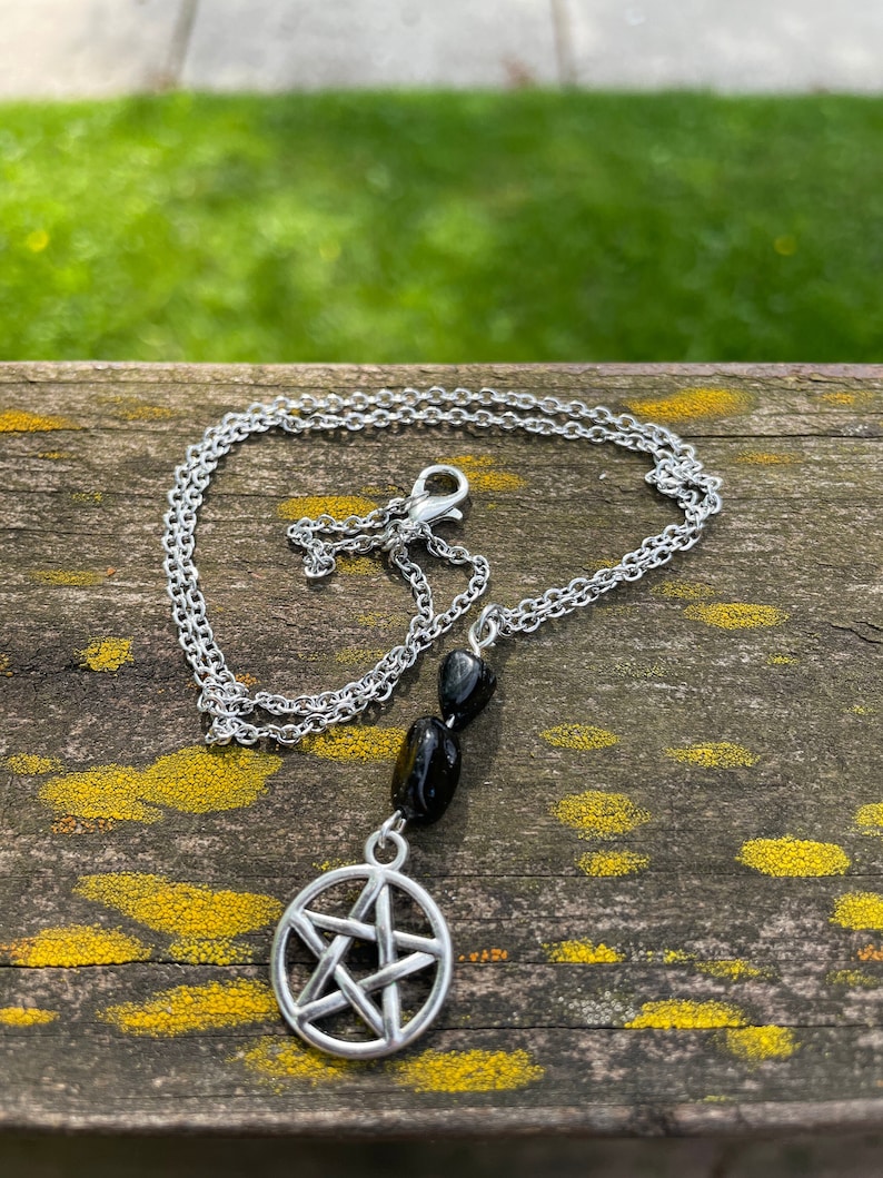 Peut inclure: Un collier en cha&icirc;ne argent&eacute;e avec un pendentif en pierre noire et un charme pentagramme argent&eacute;.
