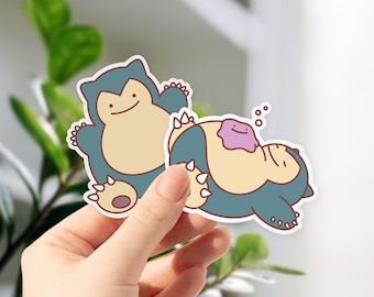 Puede incluir: Dos pegatinas de dibujos animados con los personajes Snorlax y Ditto. Snorlax se muestra sentado, y Ditto está acostado encima de Snorlax. Las pegatinas tienen una combinación de colores azul, beige y morado con un borde blanco.