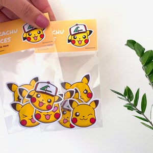 Puede incluir: Una bolsa de plástico transparente que contiene varias pegatinas amarillas con caras de Pikachu. Las pegatinas tienen orejas negras, mejillas rojas y diversas expresiones. La bolsa tiene un encabezado amarillo que dice "PIKACHU FACES STICKER PACK".