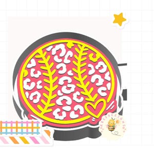 May include: A baseball-themed design featuring a pink baseball with yellow stitching and a leopard print pattern. A yellow heart is on the side. The design is surrounded by a black border and includes a small star and decorative tape.