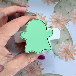 May include: A light green ghost-shaped cookie cutter with a smooth, flat top surface and a white base. The cutter features a classic ghost silhouette with rounded edges and a defined, raised border, designed for cutting dough into a ghost shape.