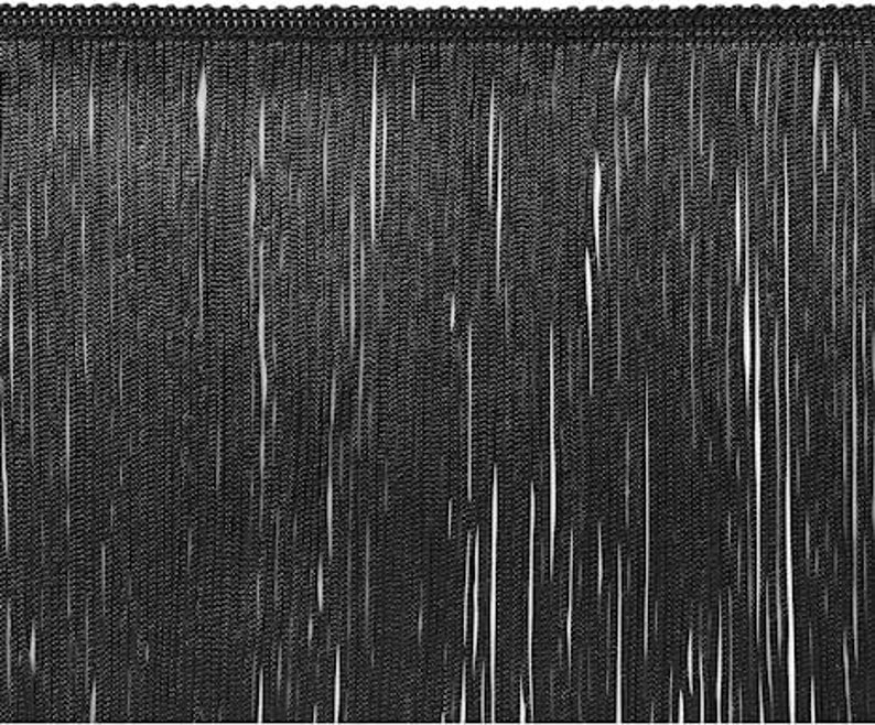 May include: Black fringe trim with a beaded top edge. The fringe is made of long, thin strands, creating a textured, cascading effect. This trim is suitable for various craft and sewing projects, adding a decorative element to garments or accessories.