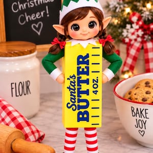 May include: A doll dressed as an elf wearing a green hat and red and white striped leggings, holding a yellow rectangular block labeled Santa's BUTTER 4oz. The elf has brown hair in pigtails with red bows and pointed ears.