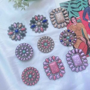 May include: Assortment of ten silver tone, round and square shaped brooches with colorful stones. The brooches feature a variety of colors including pink, blue, green, and white.