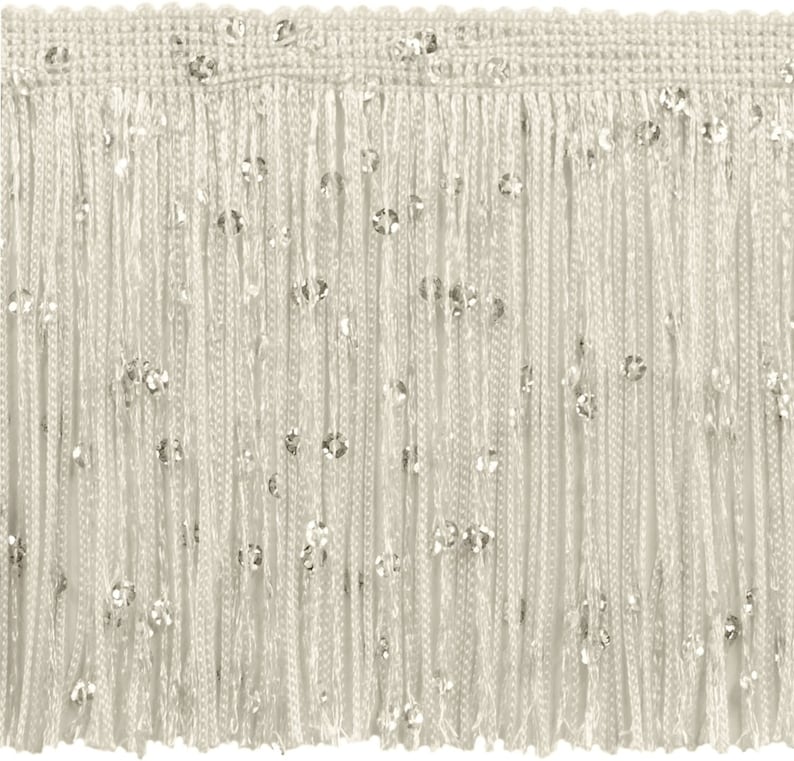 May include: Ivory fringe trim with scattered silver sequins. The trim features a woven top edge and long, dangling strands of fringe. This decorative trim is suitable for embellishing clothing, accessories, or home decor projects.