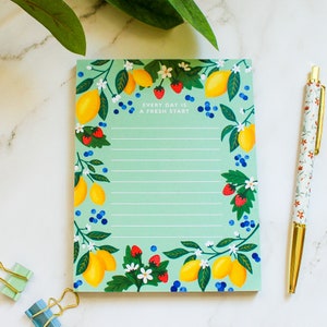 May include: A green notepad with a lemon and strawberry design. The notepad has lined pages and the text "Every day is a fresh start".