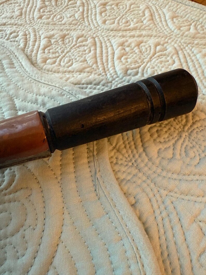 May include: A dark brown wooden object with a cylindrical shape, featuring a lighter brown section at one end. The object has a smooth, polished appearance and appears to be a handle or part of a larger tool.