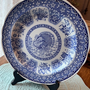 以下が含まれることがあります： 七面鳥のデザインが施された青と白のセラミック製のディナー皿。皿は波状の縁取りと花柄が特徴です。
