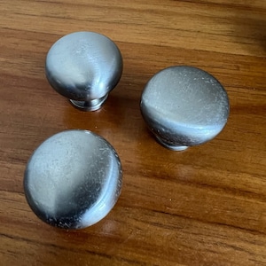 以下が含まれることがあります： ブラシ仕上げの銀色の丸いキャビネットノブが3つあります。