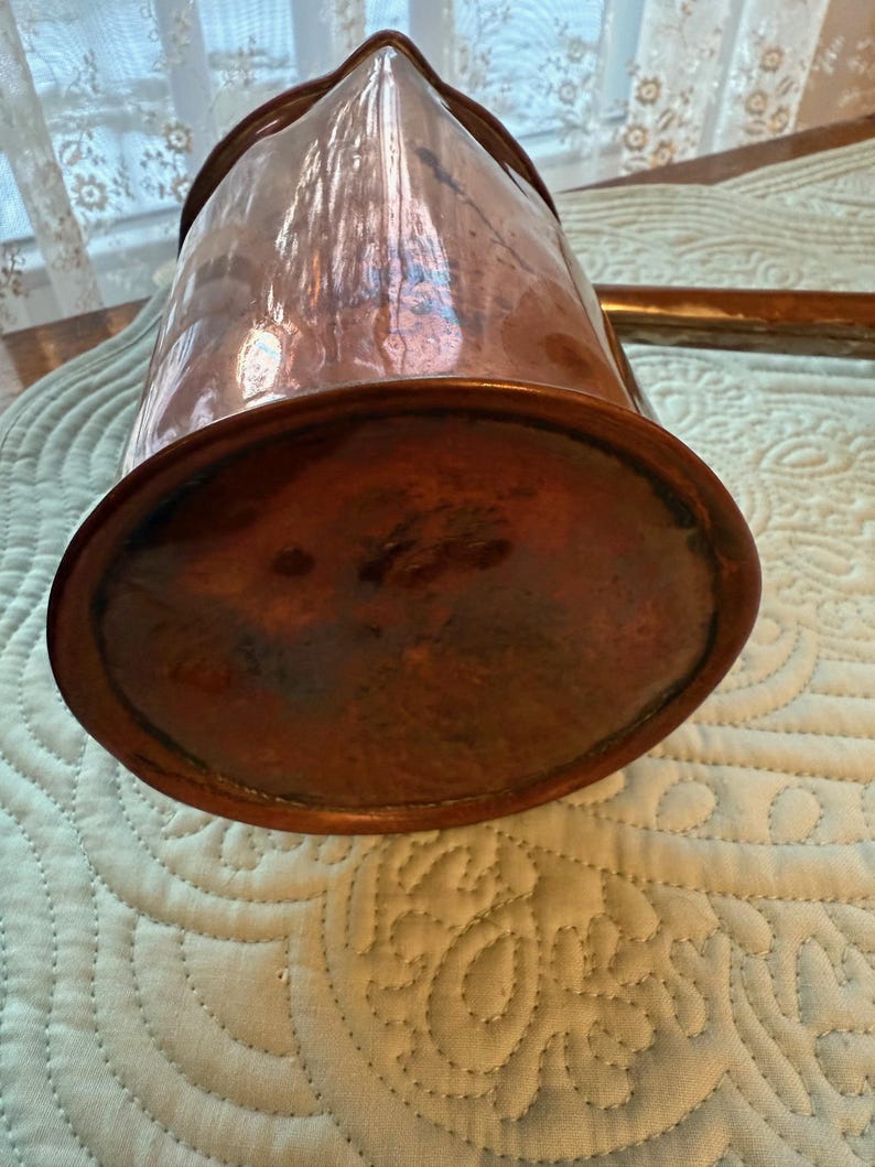 May include: A copper pitcher with a spout and handle. The pitcher has a rounded base and a polished, reflective surface. The copper has a warm, reddish-brown hue, and the pitcher appears to be vintage or antique.