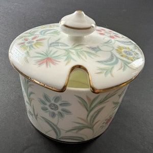 May include: A white porcelain sugar bowl with a lid and a gold trim. The bowl and lid are decorated with a floral pattern in shades of green, blue, pink, and yellow.