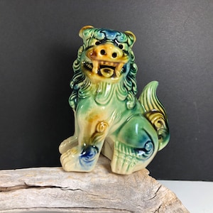 May include: A green, blue, and yellow ceramic foo dog figurine. The foo dog is sitting with its mouth open and its tail curled around its legs.