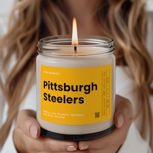 May include: A yellow and black candle with the text "Pittsburgh Steelers" and "Smells Like Primanti Brothers and Heinz Ketchup".