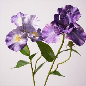 Könnte beinhalten: Zwei künstliche Irisblüten mit gewellten Blütenblättern in tiefem Violett und hellem Lavendel, mit gelben Akzenten an der Basis der Blütenblätter, grünen Stielen und grünen Blättern sowie einer kleinen, ungeöffneten Blütenknospe am rechten Stiel.