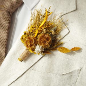 May include: A beige linen suit jacket with a brown burlap tie and a dried flower boutonniere with yellow and white flowers.
