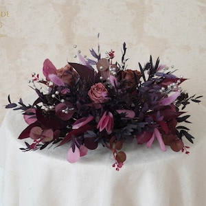 May include: A floral arrangement featuring burgundy, purple, and pink flowers and foliage. The arrangement includes roses, eucalyptus, and other decorative elements. The text "PERFECTBRIDE WEDDING" is visible in the upper left corner.