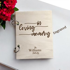 May include: A light-coloured wooden memory book with metal ring binding. The cover is engraved with the words "Loving in Memory" and "The Williams Family". The word "Engraved" is also visible.