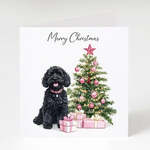 May include: A Christmas card with a black dog wearing a pink collar, beside a decorated Christmas tree and wrapped gifts. The card has the words "Merry Christmas" written in cursive.