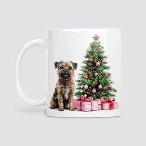 May include: White ceramic mug with a watercolour illustration of a dog wearing a red collar, a decorated Christmas tree, and wrapped gifts. The tree has red and pink baubles and a star.