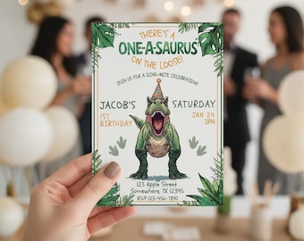 May include: A birthday invitation with a green dinosaur wearing a party hat. The invitation reads "There's a One-A-Saurus on the Loose!" and includes the text "Jacob's 1st Birthday" and event details. The invitation is held in front of a blurred background.
