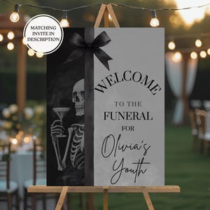 以下が含まれることがあります： 葬儀のウェルカムサイン。白黒のデザインです。サインには「オリビアの若さのための葬儀へようこそ」と書かれています。左側にはマティーニグラスを持った骸骨がいます。上部には黒いリボンが付いています。