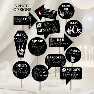 Può includere: Una collezione di 13 cartelli neri per photo booth con testo bianco. I cartelli hanno varie forme, tra cui frecce e fumetti. Il testo include "Life of the Party", "Sip Sip Honey!", e "Official Cake Tester".