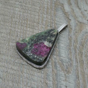 Op de afbeelding: Een driehoekige hanger met een groene en roze edelsteen in een zilveren frame.