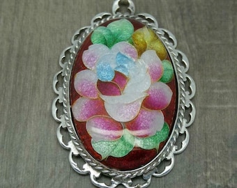 Op de afbeelding: Een zilveren hanger met een bloemenontwerp in rood, wit, groen en blauw email.