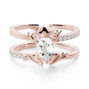 May include: Rose gold ring with a clear, pear-shaped gemstone. The ring has a deer-like design with small white stones set along the band. The inscription "G14K" is visible on the band.