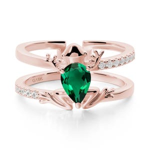 May include: Rose gold ring with a pear-shaped emerald gemstone. The ring features a double band design, with a row of small white gemstones on the upper band. The lower band has a floral design. The ring is marked with "G18K".