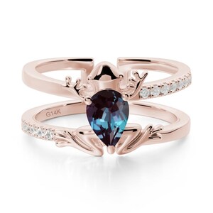 May include: Rose gold ring set with a pear-shaped alexandrite gemstone that changes colour. The ring has an antler design and a band with small, sparkling stones. The inscription "G14K" is visible on the band.