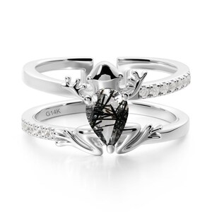 May include: A two-piece silver ring set. The top ring features a row of small, clear stones. The bottom ring has a pear-shaped, black and clear gemstone with a deer antler design. The bottom ring is stamped with "G14K".