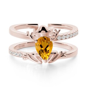 May include: Rose gold ring set with a pear-shaped, golden-yellow gemstone. The ring features an unusual design with antler-like details and small, clear stones. The band is marked with "G14K".