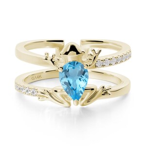 May include: A gold ring featuring a light blue, pear-cut gemstone. The ring has a double band design, with small white gemstones set along the top band. The ring is marked with "G14K".