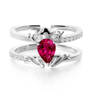 Può includere: Un set di anelli d'argento in due pezzi. L'anello inferiore presenta una pietra preziosa rosso scuro a forma di pera. L'anello superiore ha una fila di piccole pietre trasparenti. Gli anelli hanno un design a forma di corna e l'iscrizione "G14K".