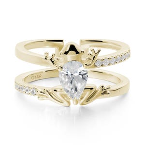 May include: A two-piece gold ring set. The top ring has a curved design with a row of small, clear stones. The bottom ring has a similar design with a pear-shaped, clear stone in the centre. The rings are connected by a decorative element.