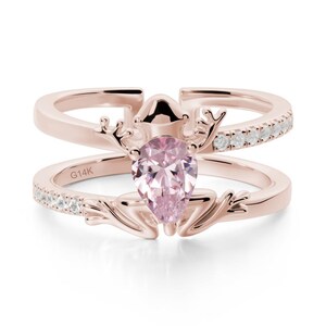 May include: Rose gold ring with a pear-shaped pink gemstone. The ring features a frog design with a band of small white gemstones. The inscription "G14K" is visible on the band.