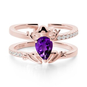 May include: Rose gold ring featuring a pear-cut, deep purple gemstone. The ring has a double band design, with small white stones set along the top band. The ring has an antler-like design around the gemstone. The text "G18K" is visible.