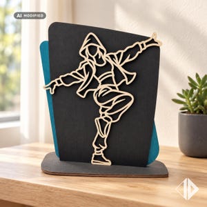 Puede incluir: Un expositor decorativo de madera con el contorno de color claro, cortado con láser, de una persona con chaqueta con capucha y pantalones holgados realizando un paso de baile, montado sobre un panel negro y azul verdoso en capas.