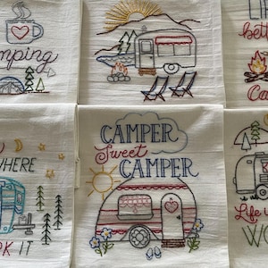 May include: Set of six embroidered kitchen towels with a camping theme. The towels feature various designs including a camper, a campfire, and a forest scene. The text on the towels includes phrases like "I love camping", "Home is where you park it", and "Life is better by the campfire".