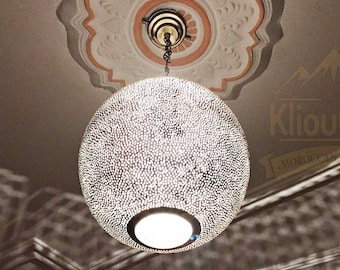 May include: A silver, round, Moroccan pendant light fixture with a decorative, patterned design. The light fixture is hanging from a chain and is suspended from a white ceiling with ornate molding.