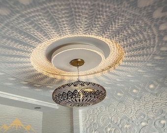 May include: A gold-toned Moroccan pendant light fixture with intricate geometric patterns hangs from a white ceiling. The light casts a decorative shadow on the ceiling.