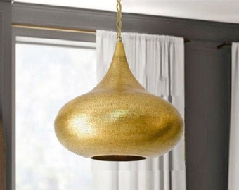 May include: A gold pendant light fixture with a teardrop shape hangs from a ceiling in a room with white curtains. The light fixture has a hammered metal finish.