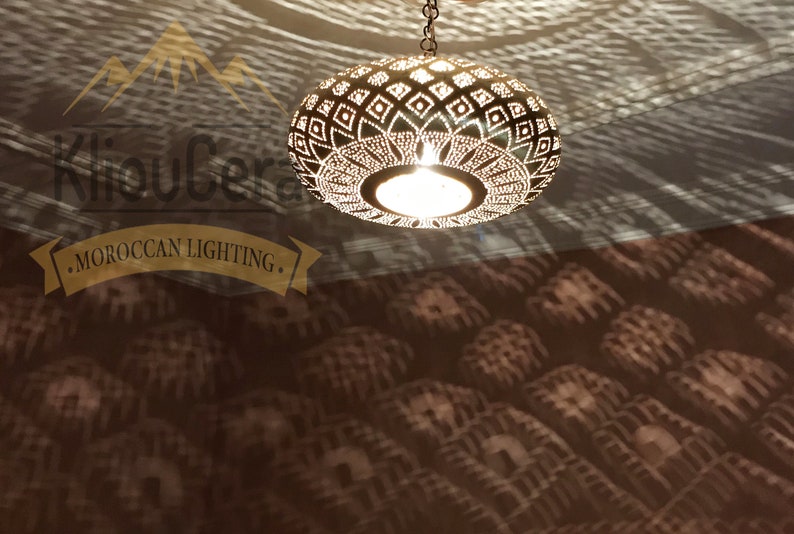 May include: A round, gold-toned Moroccan pendant light with a geometric pattern. The light is hanging from a chain and casts a shadow on the ceiling.