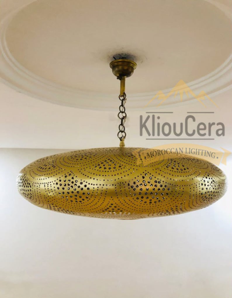 May include: A gold-toned, round, Moroccan-style ceiling light fixture with a decorative, perforated design. The light fixture is suspended from the ceiling by a chain.
