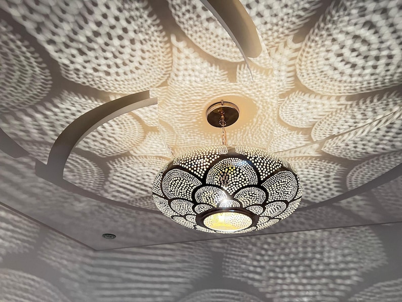 May include: A round, silver-toned pendant light fixture with a geometric pattern. The light casts a patterned shadow on the ceiling.